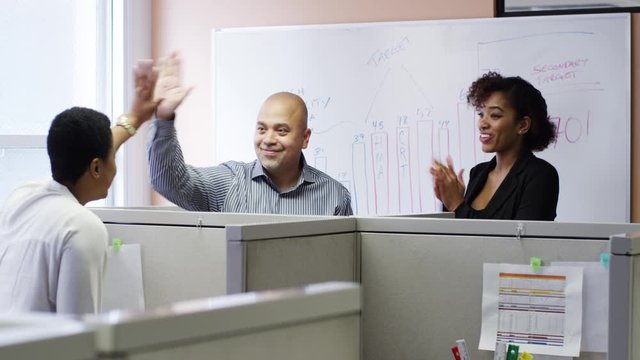 Business people high-fiving in meeting at office cubicles