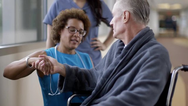Doctor shaking hands with patient in wheelchair in hospital corridor