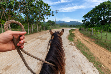 Horseback Riding on a dirty trail in the country side near a small Cuban Town during a vibrant sunny day. Taken in Trinidad, Cuba.