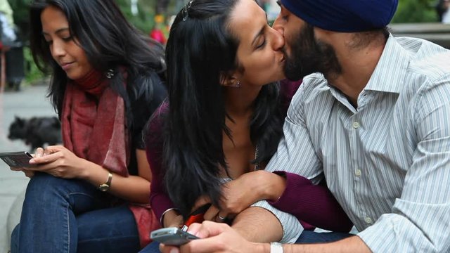 Couple kissing at fountain while friend is texting on cell phone