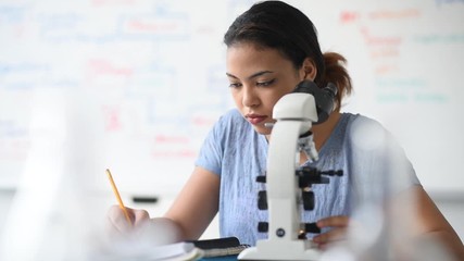 Hispanic woman using microscope and writing notes