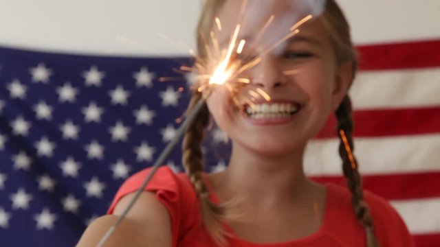 Caucasian girl waving sparkler near American flag