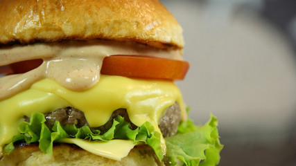 Big juicy cheeseburger with salad and sauce close up