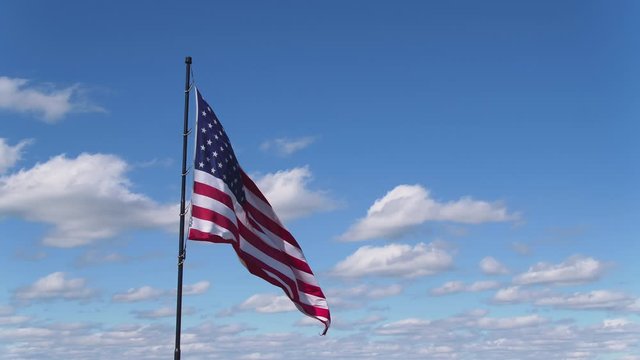 American flag blowing in the wind in blue sky with clouds