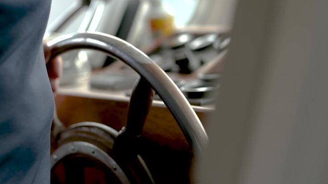 Handheld close-up shot of an old man's hand holding a boat's steering wheel