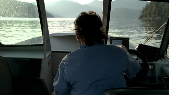 Static shot from behind a man driving a fishing boat in a river surrounded by mountains