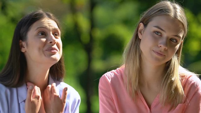 Young blonde tired of talkative best female friend during rest in park, boredom