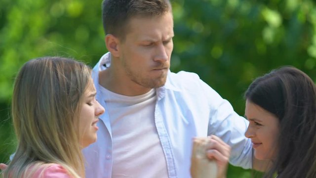 Two jealous female friends hardly fighting for handsome man trying to calm down
