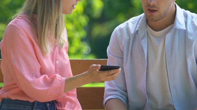 Angry woman holding boyfriends cellphone and arguing, mistrust and betrayal