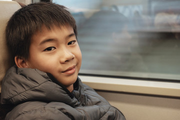 Portrait of tween mixed Asian boy in public train, preteen travel tourist on vacation in Japan winter