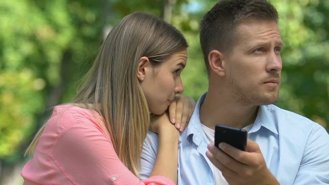 Guilty girlfriend trying to reconcile with offended male scrolling on cellphone