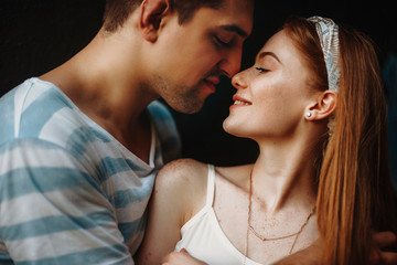 Close up of a young couple with their head touching against a black wall. Romantic young couple smiling before kissing.