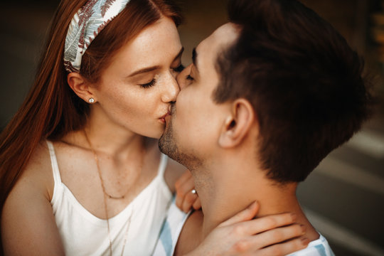 Close up of a young loving couple kissing with closed eyes. Charming young woman with red hair and freckles kissing her boyfriend outdoor while dating.