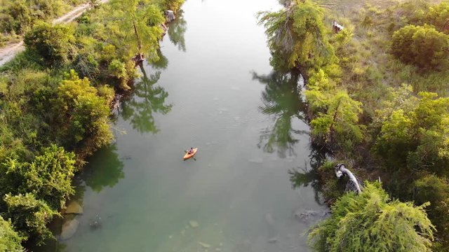 Flying above 2 kayakers as the paddle downstream at sunset. Panning upwards to reveal larger portions of the river. Aerial footage of Blanco river - Wimberly, TX