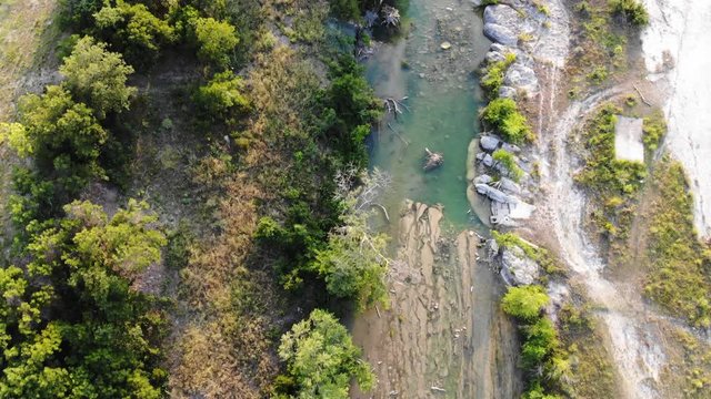 Top down view, flying up river at sunset, water is a deep green/blue. Large limestone sections visible where water carved path. - Aerial footage of the Blanco river in Wimberly, TX