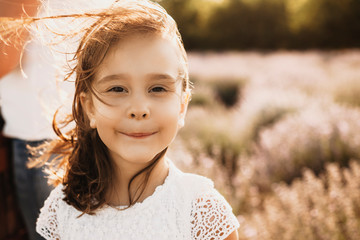 Close up portrait of a lovely little girl smiling outside. Kid looking at camera smiling against sunset while wind blowing her hair.