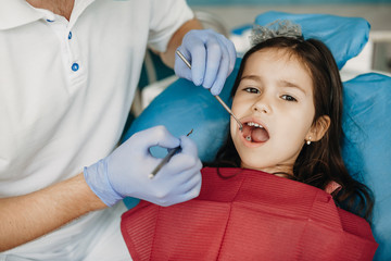 Cute little girl having a toothache doing teeth examination at pediatric dentist.