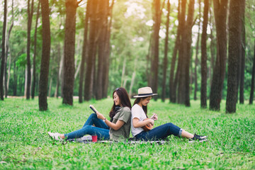 Two women playing ukulele and reading book together in the woods