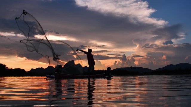 Slow Motion Silhouette of fishermen throwing fishing net during sunset with boats at the lake. Concept Fisherman's life style. Lopburi, Thailand.