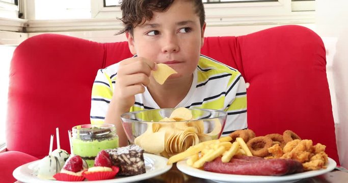 Portrait ofa caucasian teenage boy sitting at home and eating unhealthy foods.