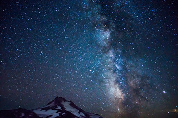 Milky Way, galaxy, and stars loom over volcanic mountain.