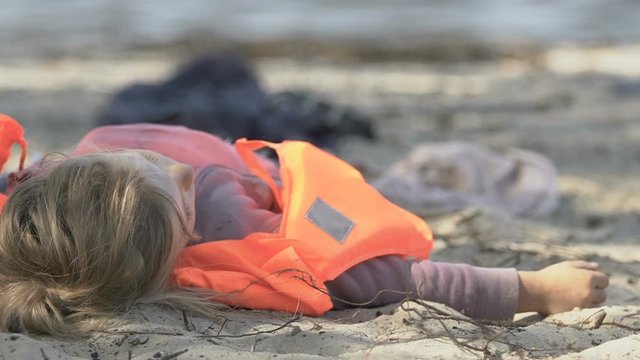 Girl in life vest lying on coast without consciousness, natural disaster victim