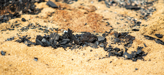 Black coals after a fire on a sandy shore.