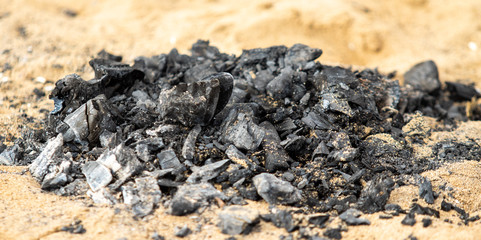 Black coals after a fire on a sandy shore.