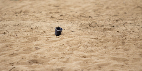 Dark, plastic cup on the sand, trash on the beach.