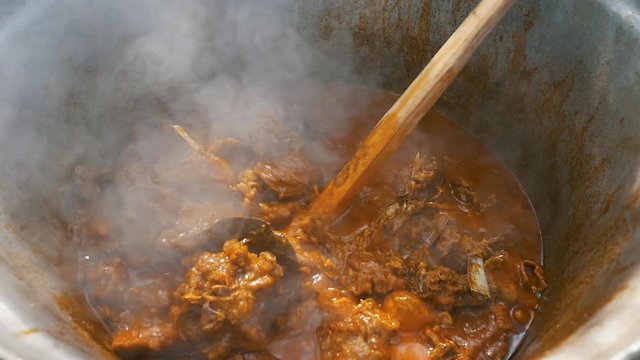 slow motion of cooking lamb stew with wooden spoon in big cauldron