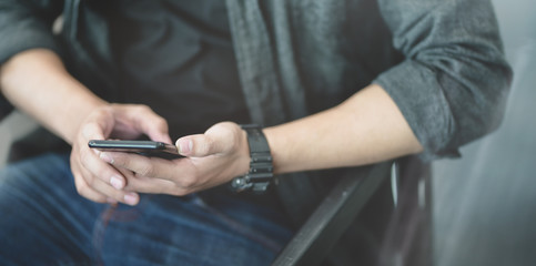 Close-up view of young man looking at his smartphone while sitting on the chair