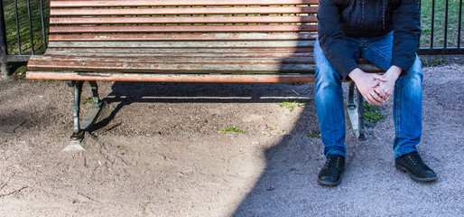 A man sitting on the street, on a bench. In place where shadow. Man sad.