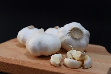 top view organic bulb garlic and clove on wooden chopping block with black background, have space for text.