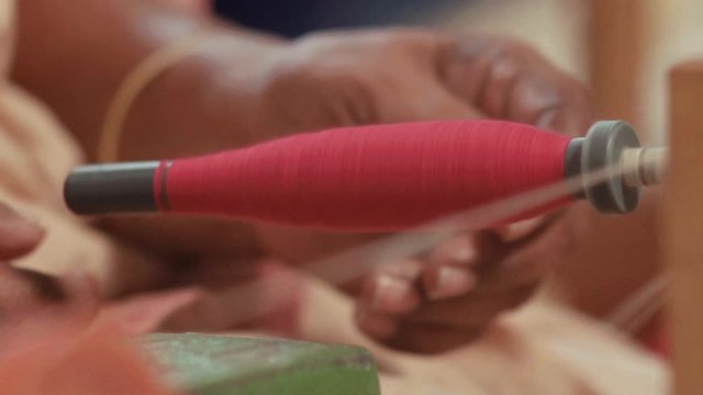 Close up of a red colored cotton thread winding on a spool guided by a hand-loom weaver for textile production