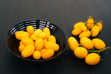 Top view, yellow cherry tomatoes in bowl on black wooden background, copy space