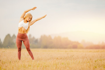 Beautiful blonde girl in white T-shirt is stretching in park field, yoga concept
