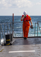 Deck Officer on ship , wearing personal protective equipment, holds VHF radio in hands.