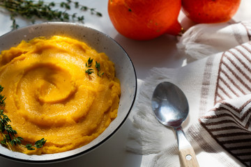 Autumn pumpkin puree in a bowl. Vegetarian autumn pumpkin cream soup with thyme on table with sunny beams. Autumnal tasty dinner or lunch