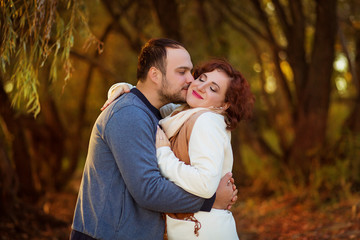 Fototapeta premium Lovers on an autumn walk in the forest, a man hugs and kisses a woman who closed her eyes.