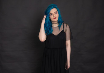 People and fashion concept - Woman dressed in black dress and blue hair posing over black background