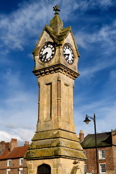 Evening light on Clock tower made of yellow Cotswold limestone with blue sky in the Town Centre of Thirsk Market town North Yorkshire England