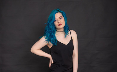 Obraz na płótnie Canvas People and fashion concept - Woman dressed in black dress and blue hair posing over black background