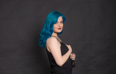 Fototapeta na wymiar People and fashion concept - Woman dressed in black dress and blue hair posing over black background with copy space