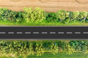 Aerial view of a road between yellow wheat fields and green trees.