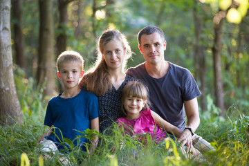 Fototapeta premium Rodzina na zewnątrz w lesie. Portret młodego ojca, matki, córki i syna outsine w zielonym lesie.