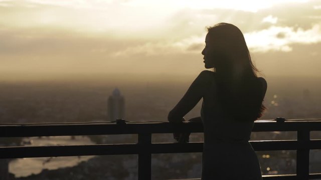 120p Slow Motion Video Of Girl Looking and staring out over the city on a balcony during sunset and cityscape in Bangkok Thailand