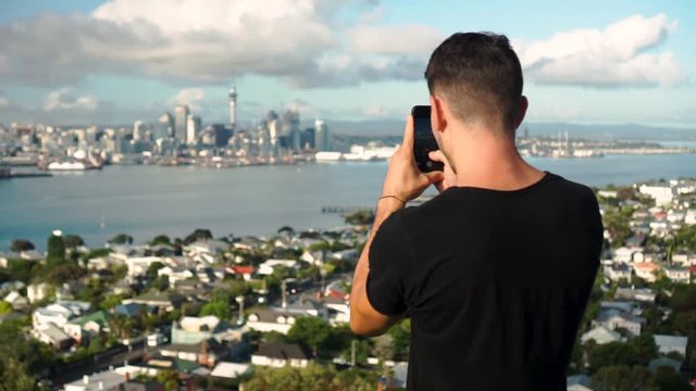 SLOWMO - Young caucasian tourist taking a photo with phone of Auckland and Sky Tower from Mount Victoria, New Zealand