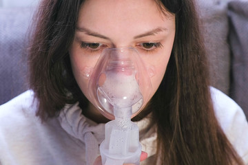 Use nebulizer and inhaler for the treatment. Young woman inhaling through inhaler mask, close-up...