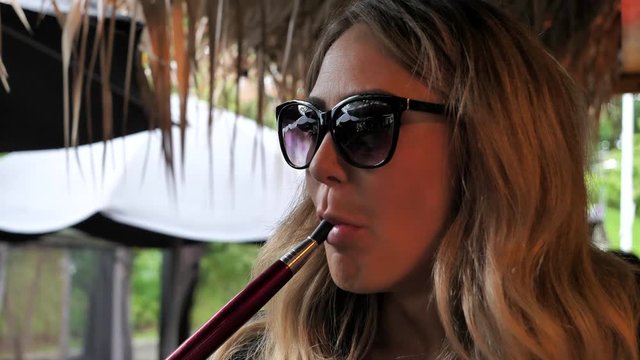 Beautiful blonde woman smoking shisha water pipe. Static. Blur