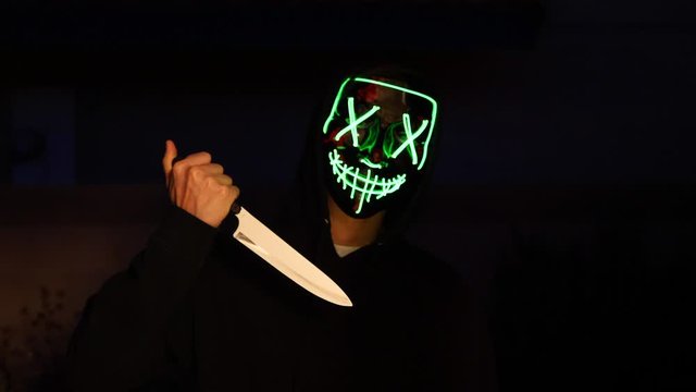 A scary slasher killer in a generic anonymous halloween horror mask pulling a knife on his murder victim.